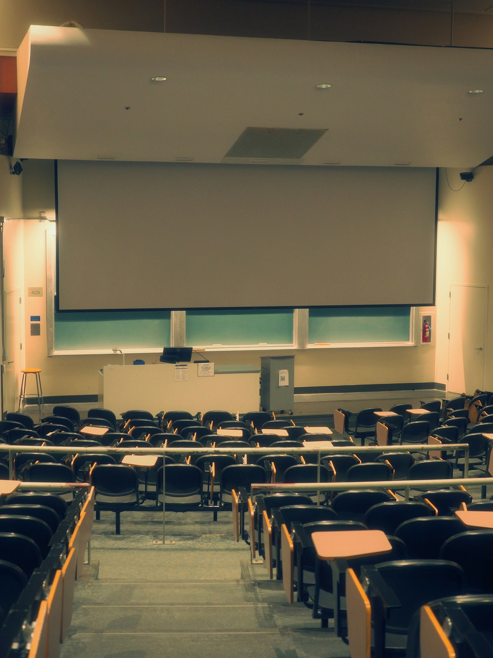 Empty lecture hall with tiered seating and a projector screen